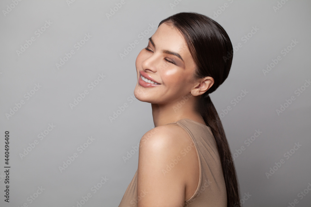 Obraz premium Pretty woman with closed eyes and dark eyebrows smiling on gray background. Attractive female model with light nude make-up, beauty photo, copy space, close up