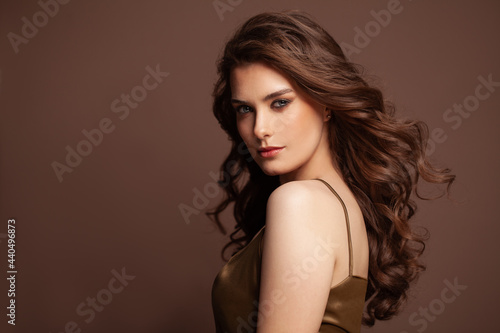 Healthy young woman with perfect skinn and long dark curly windy hair on brown background