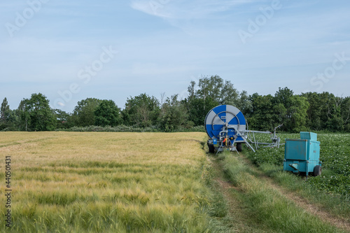 Irrigation hose reel, Agricultural Travelling Irrigator or Hose Reel Irrigation Sprinkler Machine with Water Sprinkler set up on barley wheat rice agricultural field on countryside in Germany.