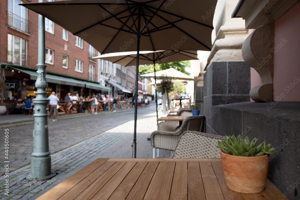 Selective focus at outdoor wooden table and chair without people under umbrella in front of Cafe, bar, and restaurant on famous walking street in old town Düsseldorf, Germany.