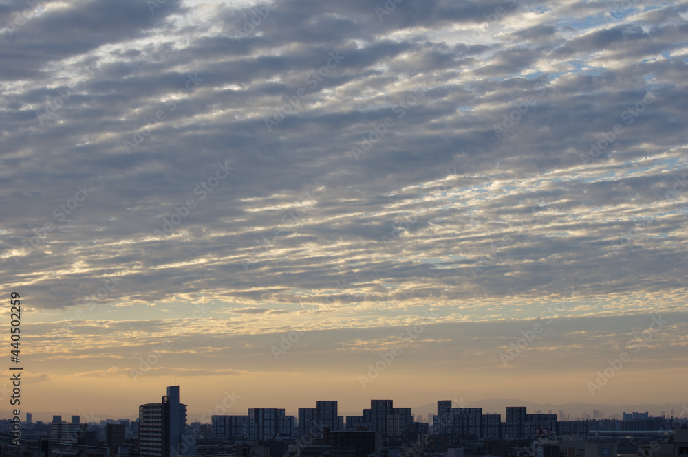  早朝、雲に覆われて太陽が見え隠れする。空と雲はブルーグレー色に。芦屋・西宮・大阪方面のビルがシルエットに浮かぶ