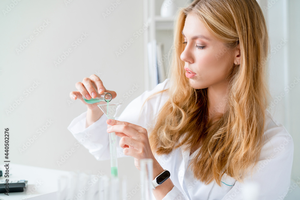 Red-haired Young woman in white medical coat, an employee of chemical laboratory, pours chemical green liquid into test tube. Red-haired Young woman in white medical coat, an employee of chemical laboratory, pours chemical green liquid into test tube.
