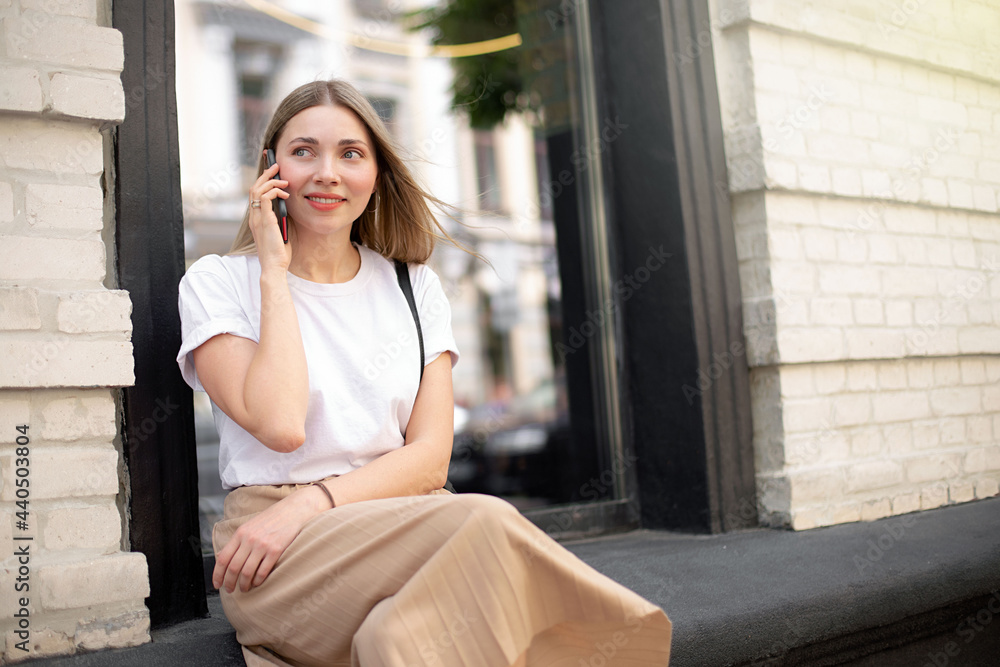beautiful caucasian girl talking on the phone while sitting outside on the background of a black window beautiful caucasian girl talking on the phone while sitting outside on the background of a black window