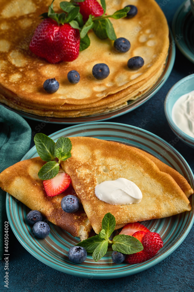 Pancakes with berries and sour cream on dark green background. Top view. Maslenitsa. Shrovetide. Shrove Tuesday. Pancake Day.