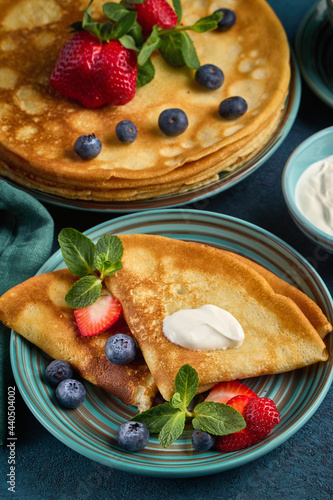 Pancakes with berries and sour cream on dark green background. Top view. Maslenitsa. Shrovetide. Shrove Tuesday. Pancake Day.