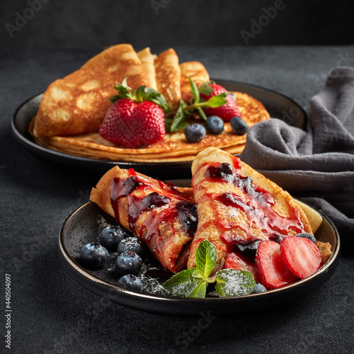 Pancakes with berries and sweet sauce on black background. Maslenitsa. Shrovetide. Shrove Tuesday. Pancake Day.