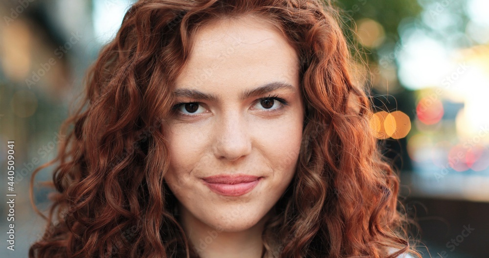 Portrait of beautiful young girl of caucasian ethnicity with curly ginger hair standing on the warm spring city street dressed at the casual clothes during morning. Portrait of beautiful young girl of caucasian ethnicity with curly ginger hair standing on the warm spring city street dressed at the casual clothes during morning.