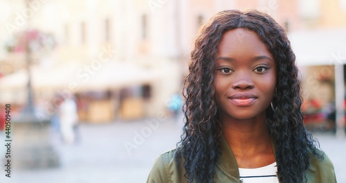 Portrait of beautiful girl of multiracial ethnicity with curly brunette hair standing on the warm spring city street dressed at the casual clothes during morning.