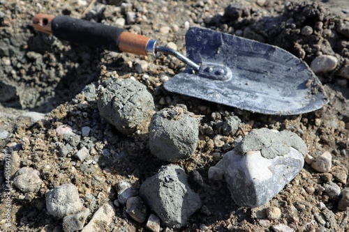 Close-up of a small steel shovel on the ground next to pieces of clay and stones.