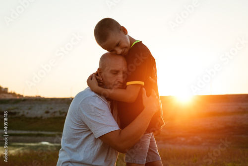 Son and dad standing against the backdrop of a colorful sunset. The relationship between father and son. Family's soulful walk in nature in the rays of the setting sun