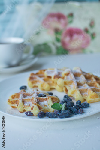 Waffles for breakfast. Belgian or Viennese waffles with berries on a white ceramic plate with a cup of aromatic coffee. 
