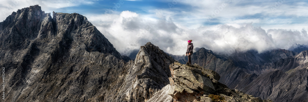 panorama young woman stands on the edge of a cliff and looks at the sky with clouds in the mountains