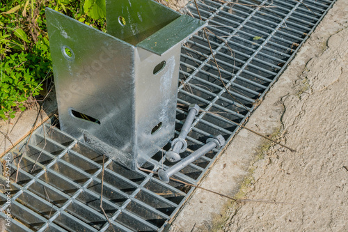 Metal box with installation bolts on metal storm grate beside concrete walkway.