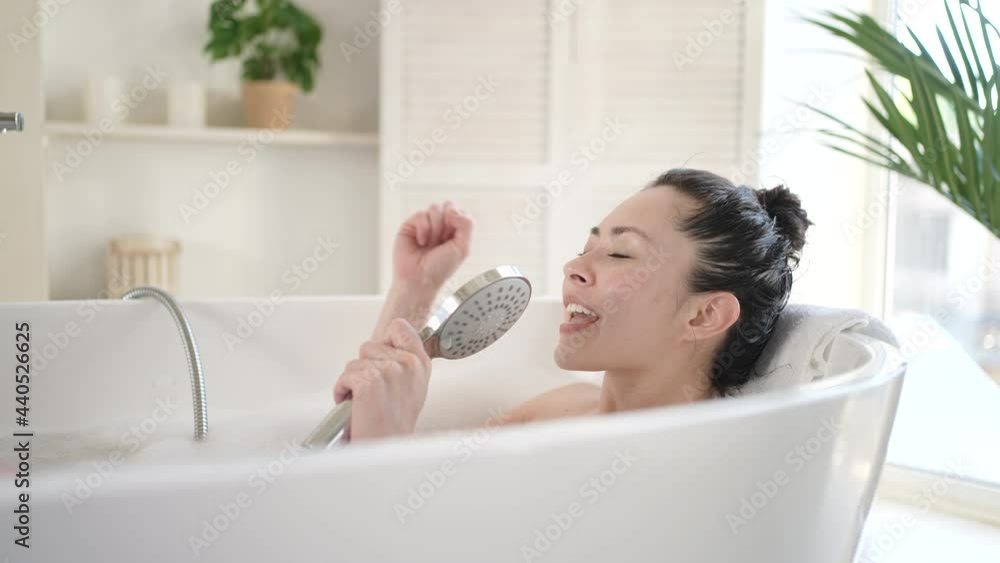 Attractive asian girl singing in bathtub using shower head. Happy millennial multi ethnic woman having fun enjoy daily bodycare in bathroom, beauty treatment therapy and healthy lifestyle concept Attractive asian girl singing in bathtub using shower head. Happy millennial multi ethnic woman having fun enjoy daily bodycare in bathroom, beauty treatment therapy and healthy lifestyle concept