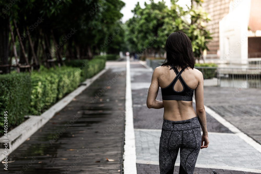 Picture of young asian women back jogging in a park. She is wearing sport bra and legging. The park has concrete floor and green leaves. Picture of young asian women back jogging in a park. She is wearing sport bra and legging. The park has concrete floor and green leaves.