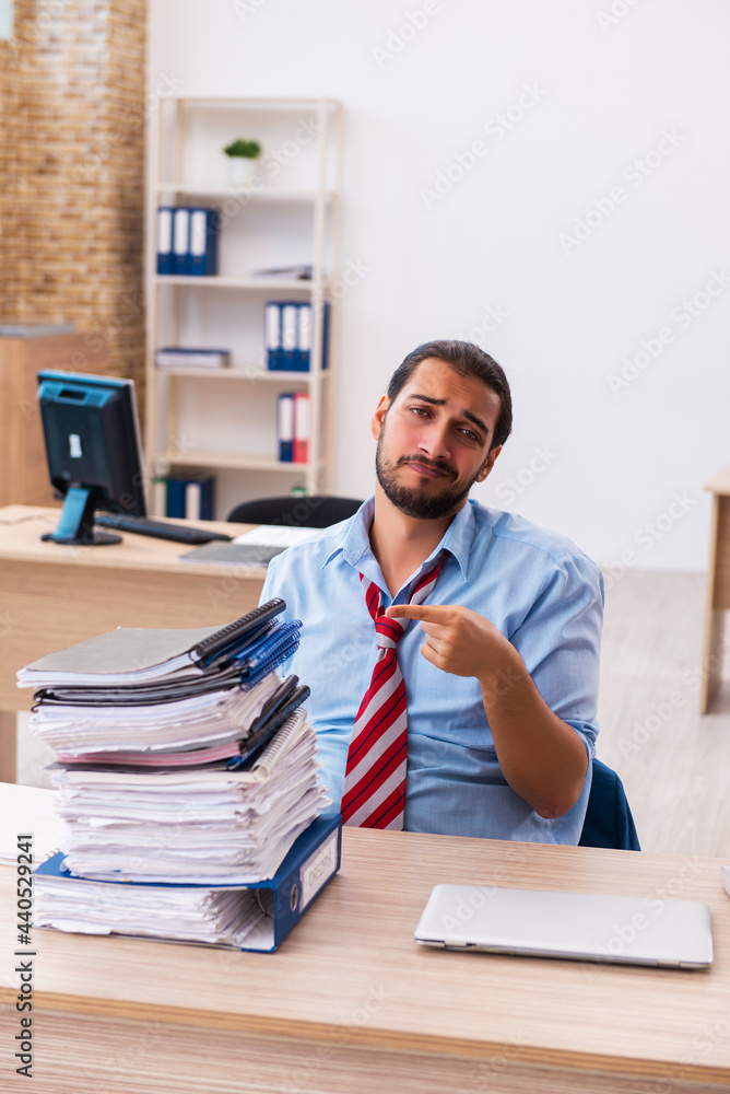 Young male employee unhappy with excessive work in the office Young male employee unhappy with excessive work in the office