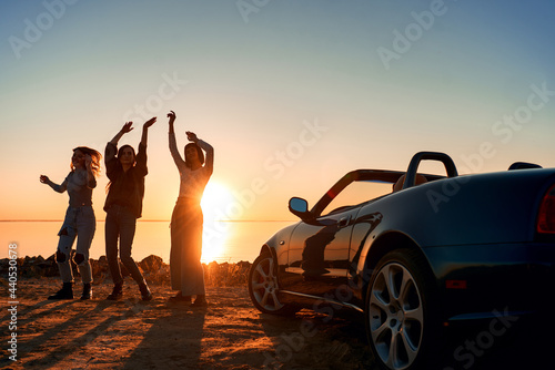 Cheerful young three women are dancing near cabriolet © Friends Stock