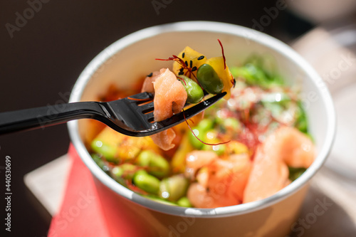 Healthy poke bowl dish with salmon and vegetables in kraft paper packaging on a wooden table. Takeout food. Fitness food. Dinner.