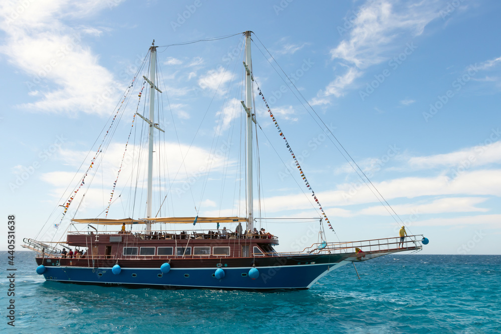 A pleasure sailboat plows the azure waters of the Red Sea, an imitation of a pirate ship, the sails are lowered, the blue sky with white clouds A pleasure sailboat plows the azure waters of the Red Sea, an imitation of a pirate ship, the sails are lowered, the blue sky with white clouds