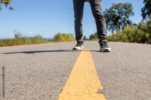 Wallpaper Mural Men`s feet standing on asphalt road with yellow marking lines. Man wearing sneakers and jeans. Torontodigital.ca