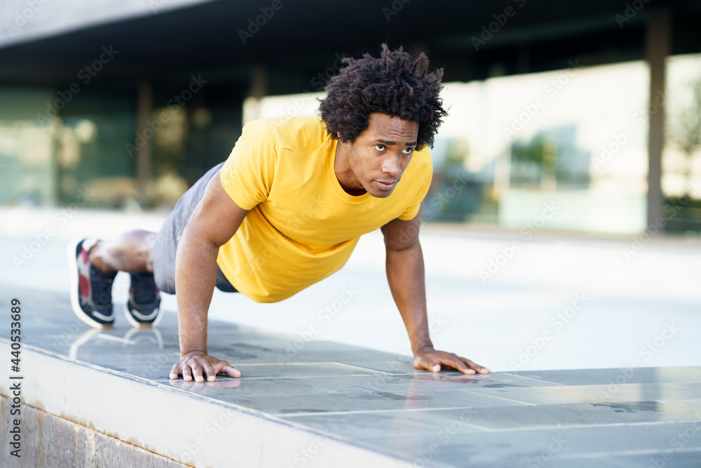 Fototapeta premium Black man doing triceps dip exercise on city street bench.