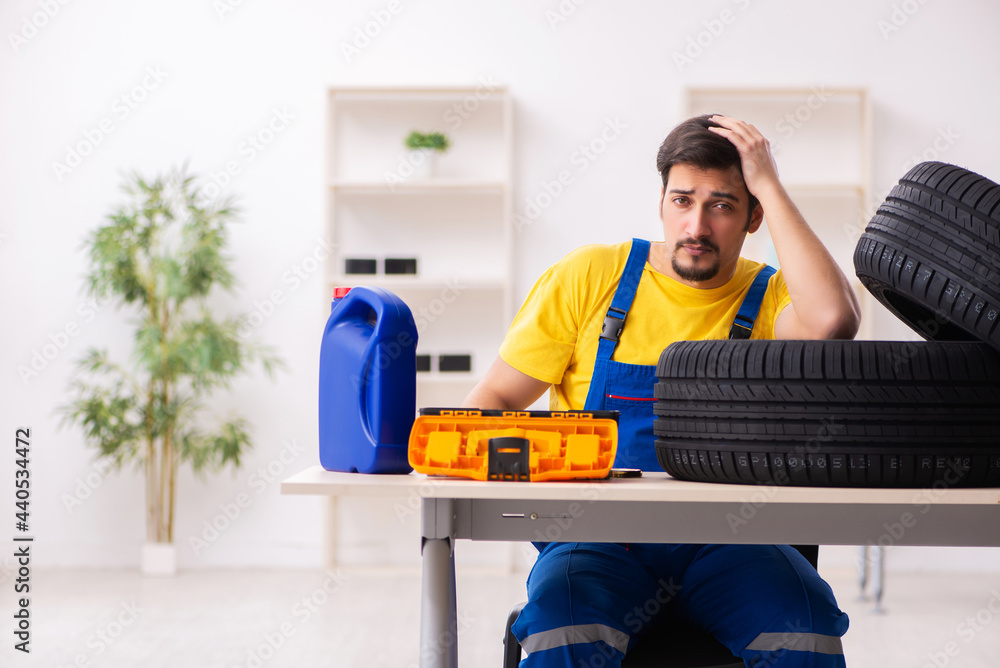 Young male garage worker with tyre at workshop Young male garage worker with tyre at workshop