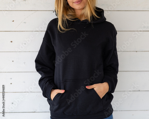 Sweatshirt hoodie mockup. Unrecognizable woman stands in a black sweatshirt against a background of white boards, facing the camera. photo