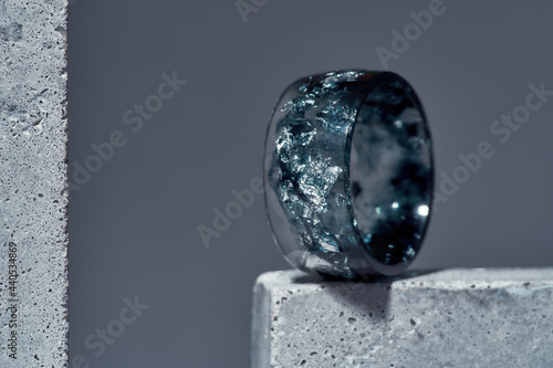 Close up of stylish ring made of dark blue epoxy resin with silver foil inside on concrete element isolated over gray background photo