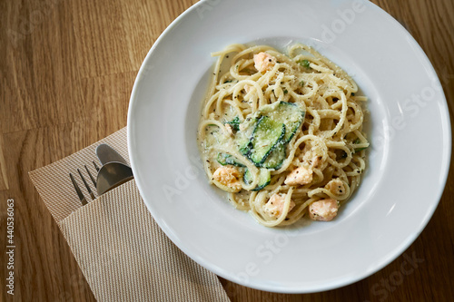 Plate of Italian pasta fettuccine in a creamy sauce with salmon and zucchini on a table