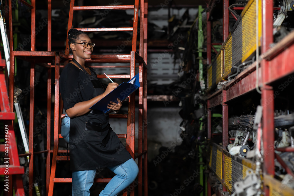 Obraz premium Plus size black female worker inspecting old car parts stock while working in automobile large warehouse