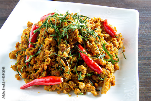 Spicy stir fry minced pork with curry paste (Thai call *Kua kling*) on dark brown wooden table photo