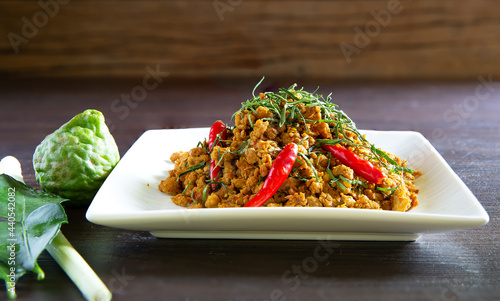 Spicy stir fry minced pork with curry paste (Thai call *Kua kling*) on dark brown wooden table