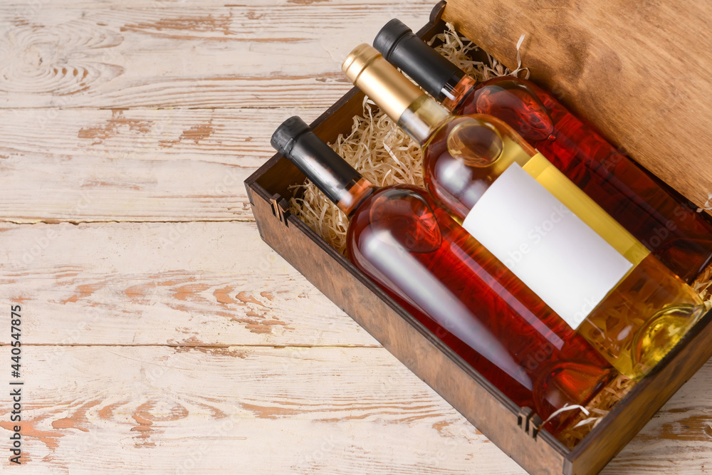 Box with bottles of wine on light wooden background