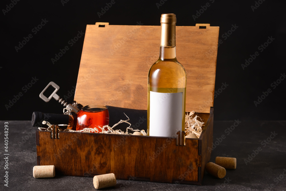 Naklejka premium Box with bottles of wine, glass and corkscrew on dark background