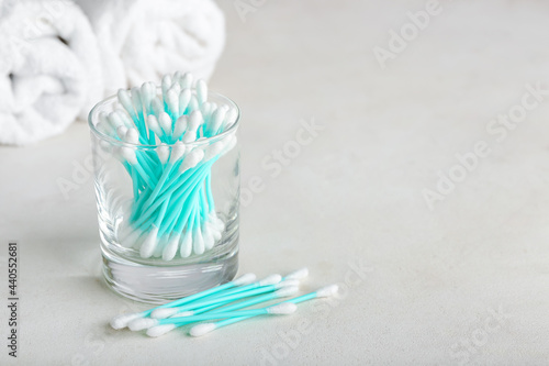 Glass with cotton swabs on light background