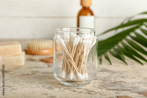 Glass jar with cotton swabs and tropical leaf on color background
