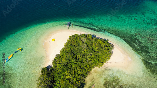 Island with a sandy beach and azure water surrounded by a coral reef and an atoll. Britania Islands, Surigao del Sur, Philippines.