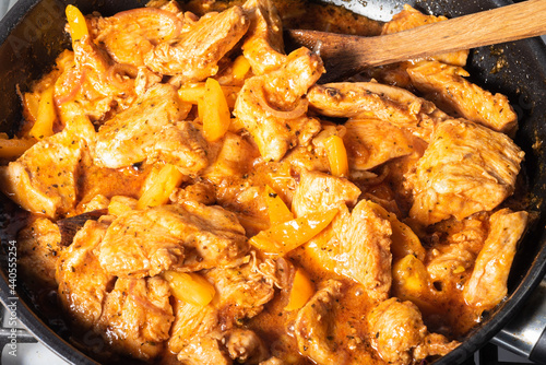 Indian style chicken cooking. Cooking traditional chicken curry. Chicken pieces are cooked in a pan and spicy curry sauce and mixed with a wooden spoon, close-up. photo