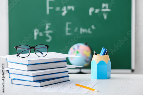 Stack of books and answer sheet forms with eyeglasses on table in classroom