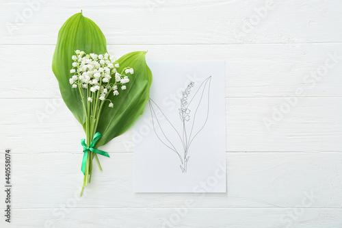 Beautiful lily-of-the-valley flowers and greeting card on light wooden background