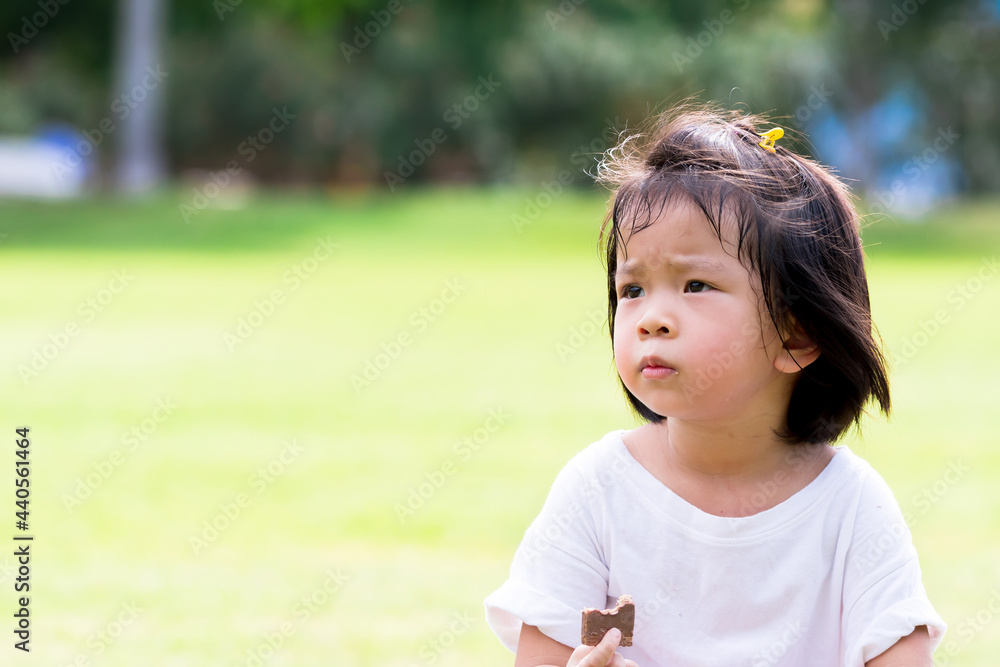 Asian child eating chocolate wafers on natural green laws background. Cute girl holding sweetmeat on her hand. Baby age 4 years old. Asian child eating chocolate wafers on natural green laws background. Cute girl holding sweetmeat on her hand. Baby age 4 years old.