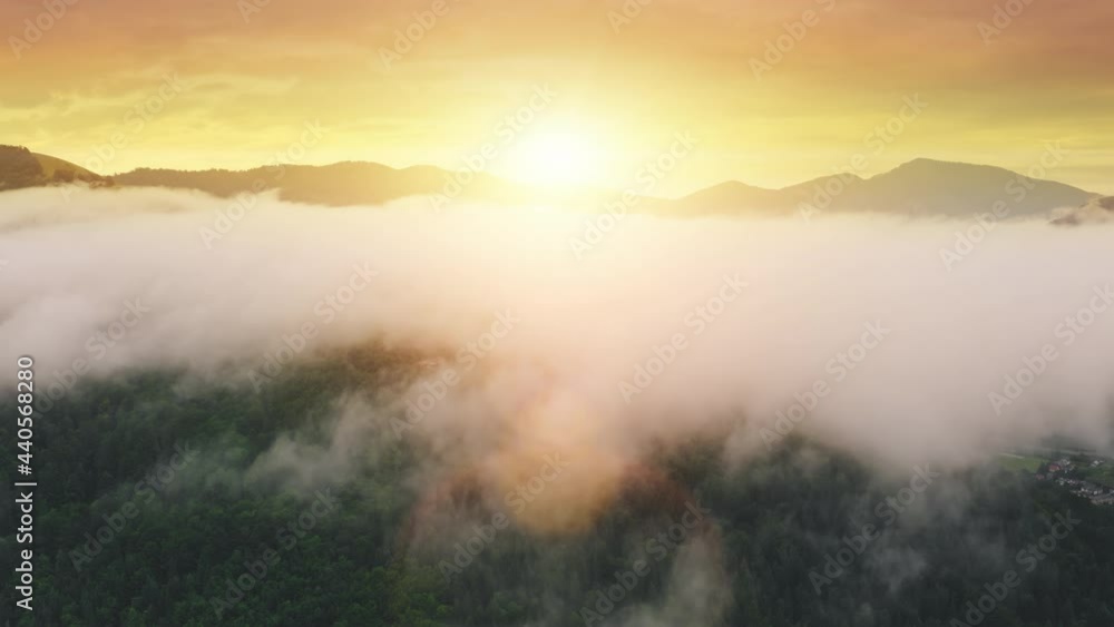 Aerial view on orange sunrise in fog Alp mountains. Morning mist over green spruce forest. Top view of mount range. Beautiful panorama of wild landscape with sun lens flare. Europe nature drone flight Aerial view on orange sunrise in fog Alp mountains. Morning mist over green spruce forest. Top view of mount range. Beautiful panorama of wild landscape with sun lens flare. Europe nature drone flight