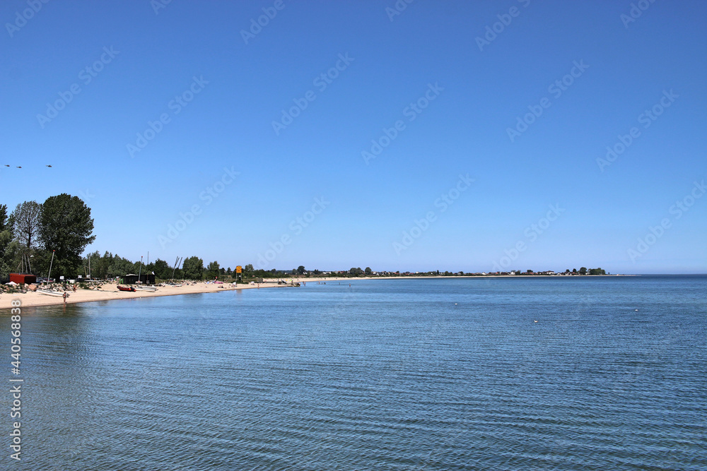 The Baltic Sea, the coast and the beach in Mechelinki in Poland. The Baltic Sea in summer. Blue sky, gulls floating on the water. People are sunbathing on the beach 
