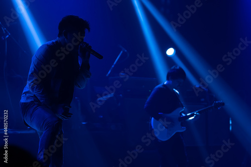 Silhouette of young Asian pop rock singer and band performing with full spectrum of light and sound at the concert. Blue light background