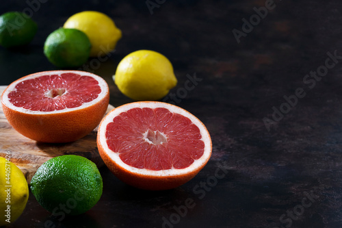 Cut pink grapefruit with lemons and limes on a dark background.