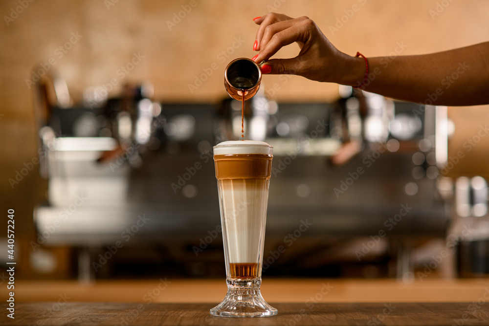 Great view of glass with syrup and whipped cream into which woman's hand pours espresso
