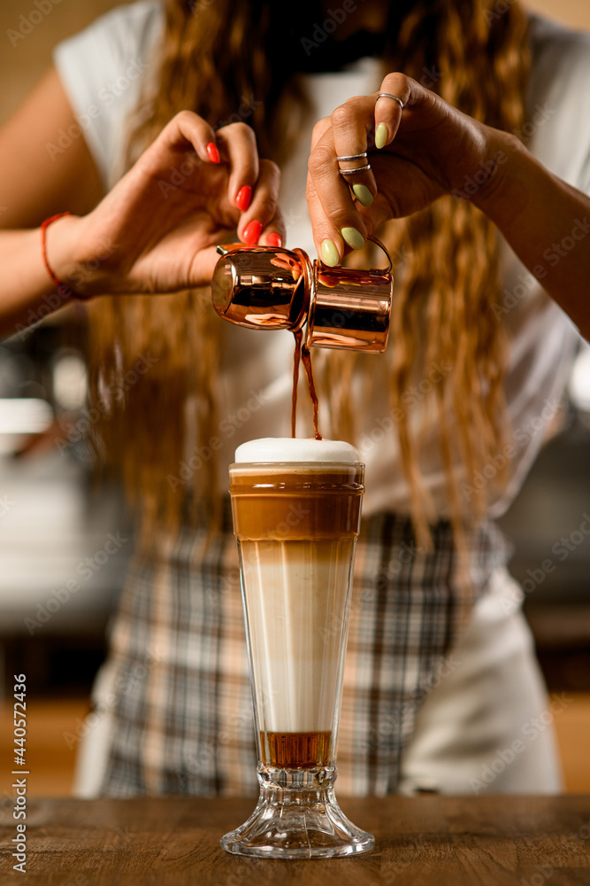 Close-up of glass with syrup and whipped cream into which barista accurate pours espresso Close-up of glass with syrup and whipped cream into which barista accurate pours espresso