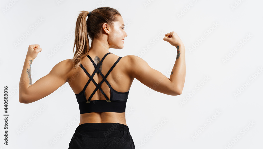 Sport and women. Rear view of strong fitness athlete, female bodybuilder,  flexing muscles, showing fit body, biceps and athletic back, smiling  satisfied, white background Photos
