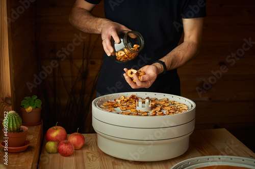 A man's hands are filling the glass jar all the way to the top with dried apple chunks. A food dried in order to be used in food and desserts for the winter. Drying food in a dehydrator. photo