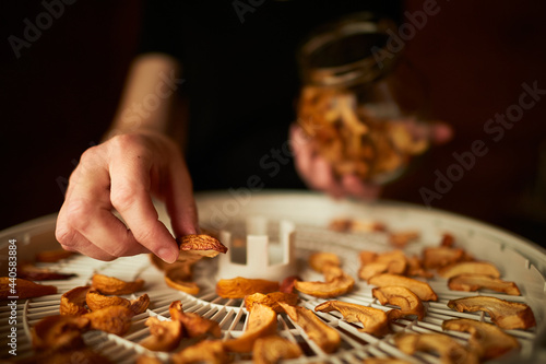 A person's hands are filling the glass jar all the way to the top with dried apple chunks. A food dried in order to be used in food and desserts for the winter. Dehydrating apples for food storage